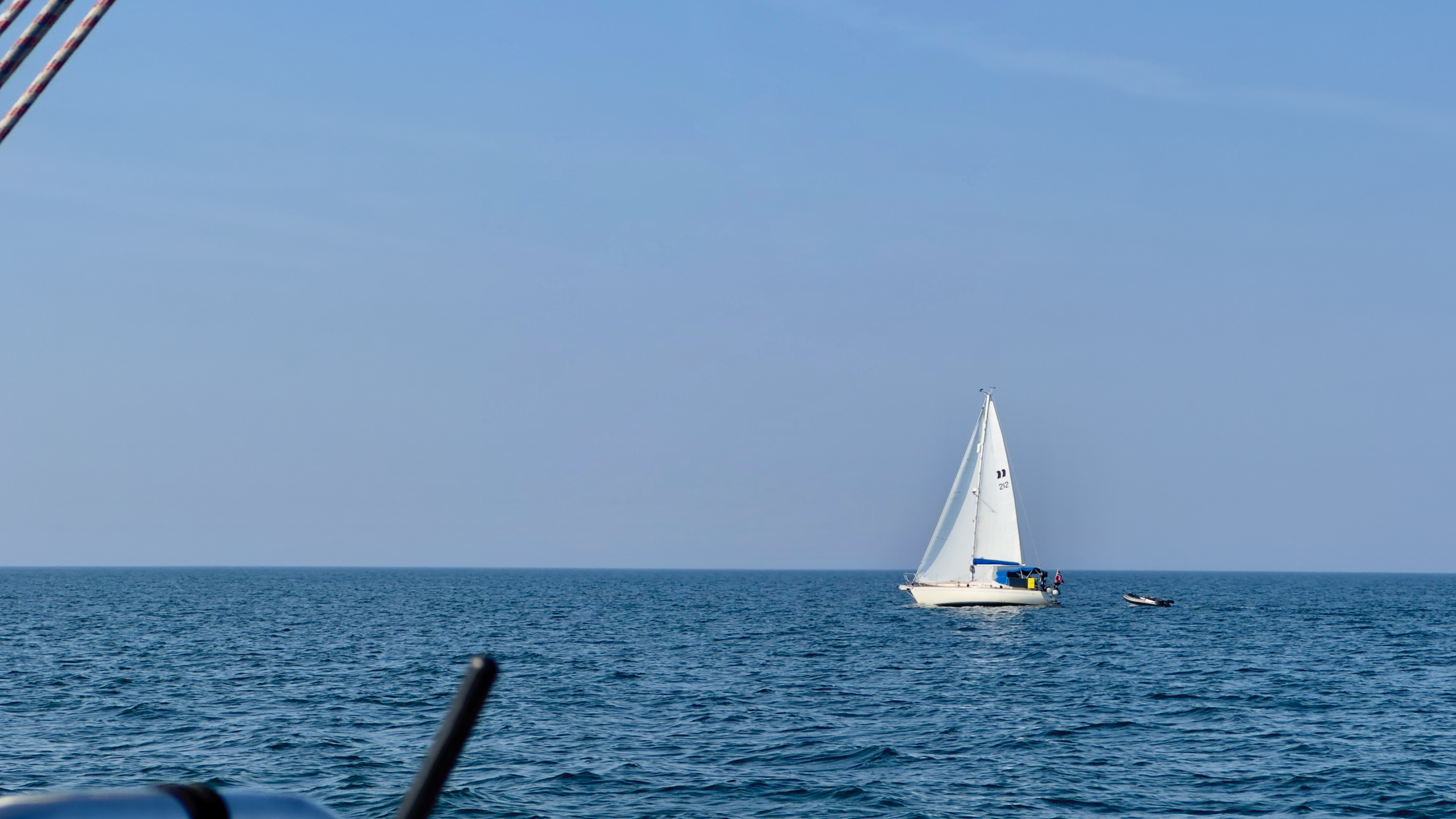 Weiße Segelyacht mit weißen Segeln am Horizont vor blauem Himmel
